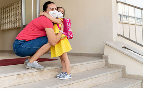 Mom hugs daughter wearing mask before school.