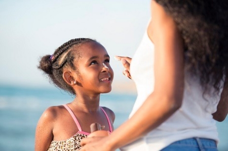 A mother applies sunscreen to her daughter while at the beach. A mother applies sunscreen to her daughter while at the beach.