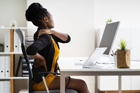 An office worker stretches uncomfortably at her desk.