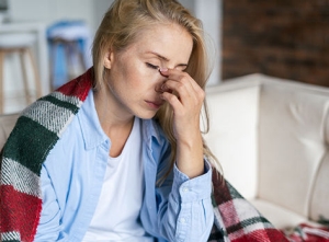 An adult woman suffering from allergfies, holds her forehead.