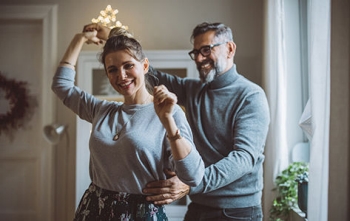 A pair of empty nesters dance together in front of a window.