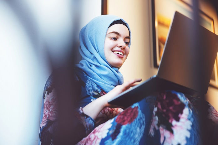 Young girl on balcony seeks behavioral health information on a laptop.