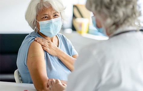 An elderly woman smiles at a nurse after receiving her flu vaccination.