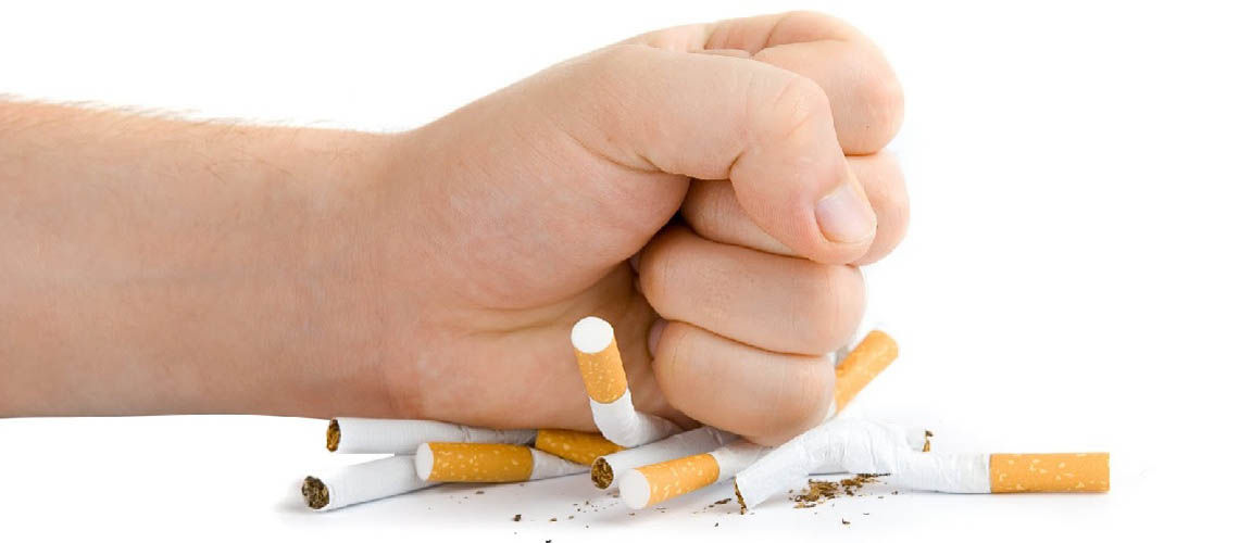 A fist crushes a pile of cigarettes.