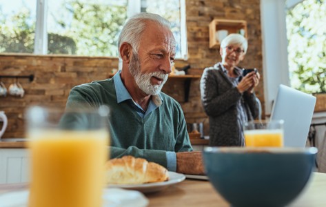 Senior man looks at laptop over breakfast.